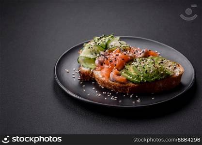 Fresh tasty sandwich with salmon, avocado and sesame and flax seeds on a dark concrete background