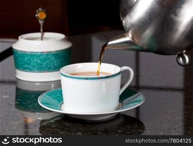 Fresh tea being poured into white cup on marble kitchen worktop