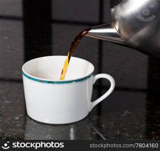 Fresh tea being poured into white cup on marble kitchen worktop