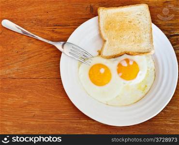 fresh toast and two fried eggs on white plate on wooden table