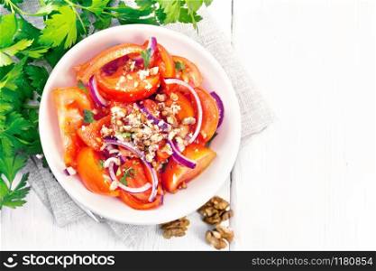 Fresh tomato salad with walnuts and red onions, seasoned with olive oil, vinegar, fenugreek and salt in a plate on a towel on a wooden board background from above