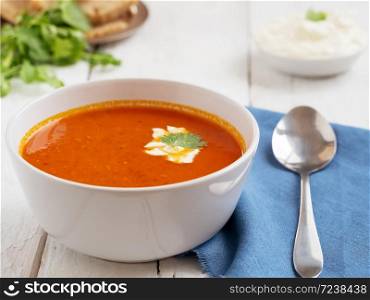 Fresh tomato soup. Seasonal summer dish. Located on a vintage white background. Nearby is a spoon on a blue cotton napkin. Bread and Sauce. Close-up.