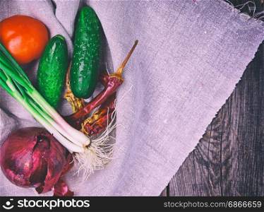 Fresh tomato vegetables, cucumbers and green onion on a gray textile napkin, top view, vintage toning