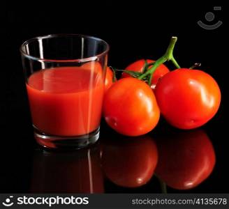 fresh tomatoes and tomato juice on black background