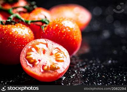 Fresh tomatoes and tomato slices on the table. On a black background. High quality photo. Fresh tomatoes and tomato slices on the table.