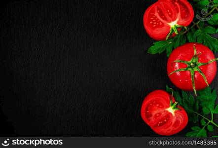 Fresh tomatoes cut in half on a black stone background. Top view with copy space. Drops of water on tomatoes