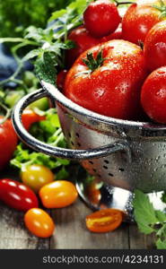 fresh tomatoes (in metal colander) and herbs on a wooden table