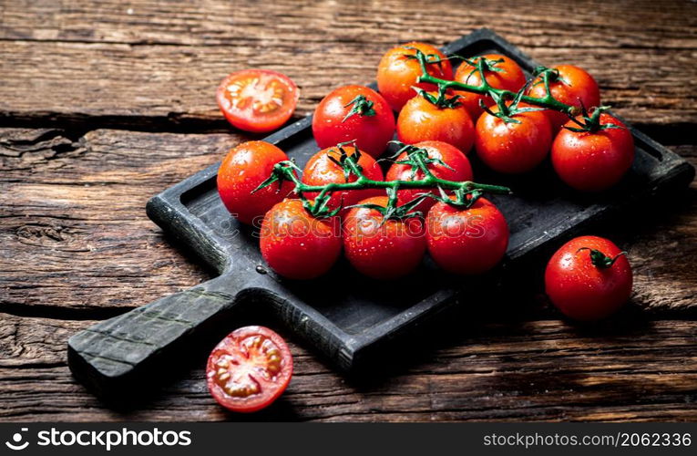 Fresh tomatoes on a branch on a cutting board. On a wooden background. High quality photo. Fresh tomatoes on a branch on a cutting board.