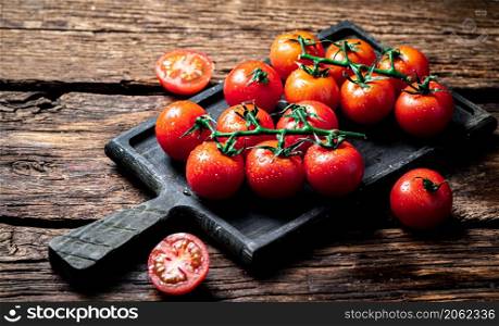 Fresh tomatoes on a branch on a cutting board. On a wooden background. High quality photo. Fresh tomatoes on a branch on a cutting board.
