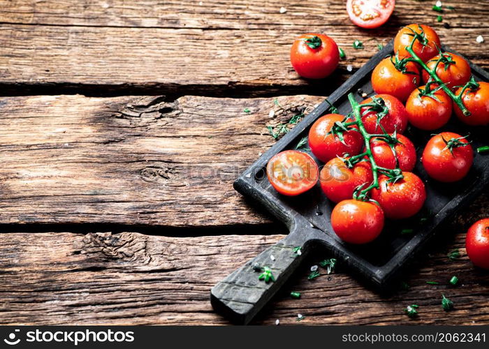 Fresh tomatoes on a branch on a cutting board. On a wooden background. High quality photo. Fresh tomatoes on a branch on a cutting board.