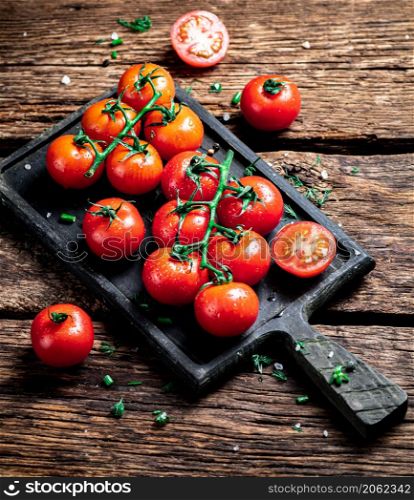 Fresh tomatoes on a branch on a cutting board. On a wooden background. High quality photo. Fresh tomatoes on a branch on a cutting board.