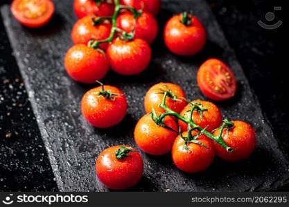 Fresh tomatoes on a branch on a stone board. On a black background. High quality photo. Fresh tomatoes on a branch on a stone board.