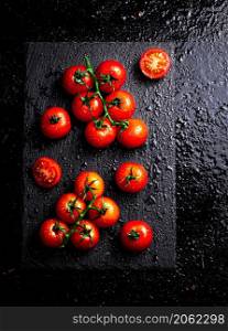 Fresh tomatoes on a branch on a stone board. On a black background. High quality photo. Fresh tomatoes on a branch on a stone board.