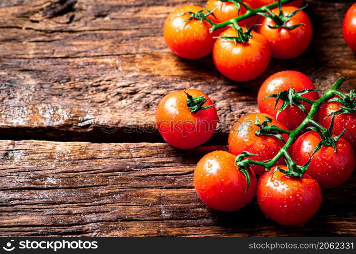 Fresh tomatoes on a branch on the table. On a wooden background. High quality photo. Fresh tomatoes on a branch on the table.