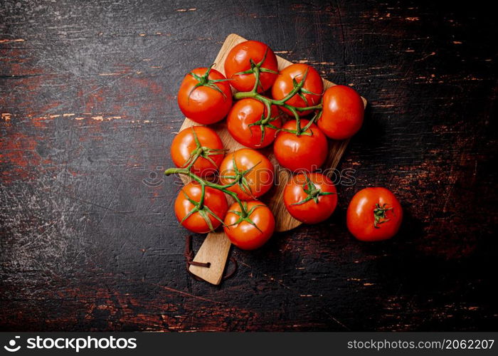 Fresh tomatoes on a wooden cutting board. Against a dark background. High quality photo. Fresh tomatoes on a wooden cutting board.