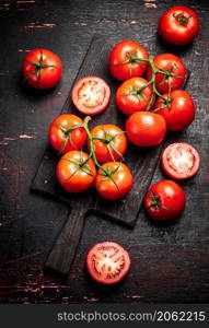 Fresh tomatoes on a wooden cutting board. Against a dark background. High quality photo. Fresh tomatoes on a wooden cutting board.