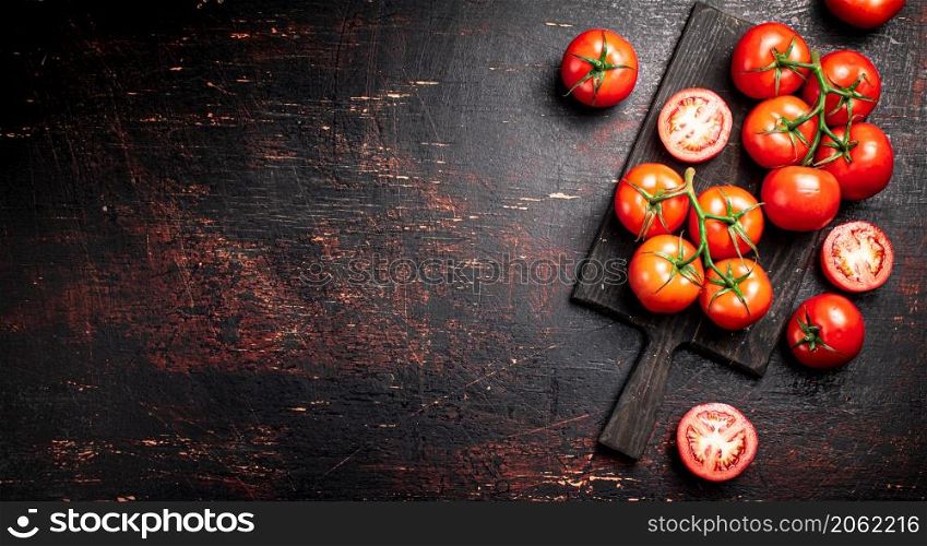 Fresh tomatoes on a wooden cutting board. Against a dark background. High quality photo. Fresh tomatoes on a wooden cutting board.