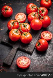 Fresh tomatoes on a wooden cutting board. Against a dark background. High quality photo. Fresh tomatoes on a wooden cutting board.