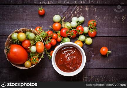Fresh tomatoes organic harvesting on basket and ketchup in cup tomato sauce on wooden dark background - top view