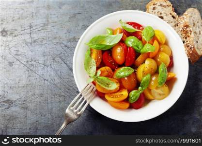 Fresh tomatoes with basil leaves in a bowl with bread and fork on vintage background.