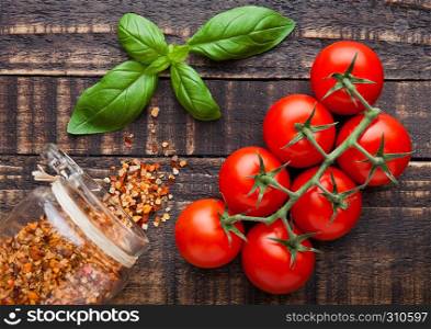 Fresh tomatoes with basiland spices jar on grunge wooden background