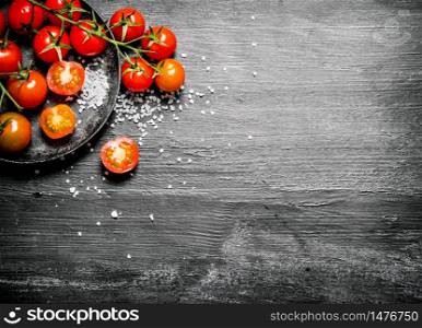 Fresh tomatoes with coarse salt . On black rustic background.. Fresh tomatoes with coarse salt .