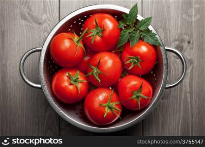 Fresh tomatoes with green leaf and waterdrops in colander on wooden background. Top view