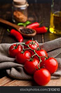Fresh tomatoes with red and black pepper on kitchen towel and kitchen board.Jar with olive oil and spices on background