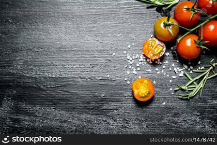 Fresh tomatoes with salt and rosemary. On black rustic background.. Fresh tomatoes with salt and rosemary.