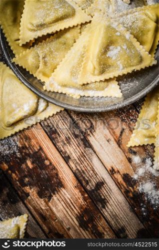 Fresh triangular ravioli in metal bowl on rustic wooden background, top view, close up