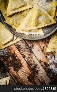 Fresh triangular ravioli in metal bowl on rustic wooden background, top view, close up