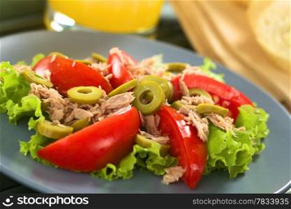 Fresh tuna, tomato and green olive salad served on lettuce leaf on blue plate with juice in the back (Selective Focus, Focus on the front of the olive in the middle of the salad) . Tuna Tomato Olive Salad