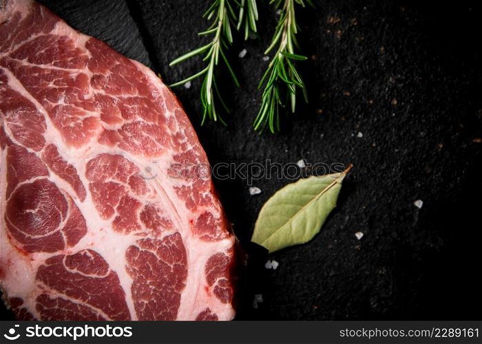 Fresh uncooked pork steak on a stone board. On a black background. High quality photo. Fresh uncooked pork steak on a stone board.
