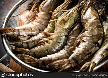 Fresh uncooked shrimp in a colander. On rustic dark background. High quality photo. Fresh uncooked shrimp in a colander.