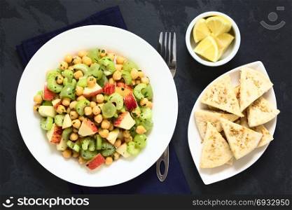 Fresh vegan chickpea, celery, grape and apple salad with parsley, homemade sesame pita chips and lemon on the side, photographed overhead on slate with natural light. Chickpea, Celery, Grape and Apple Salad