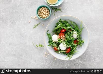 Fresh vegetable Caprese salad with arugula, tomato, pine nuts and mini mozzarella cheese. Top view