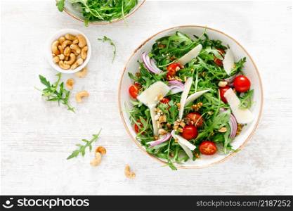 Fresh vegetable salad with arugula, tomato, onion, parmesan cheese and cashew nuts. Top view