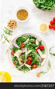 Fresh vegetable salad with arugula, tomato, onion, parmesan cheese and cashew nuts. Top view