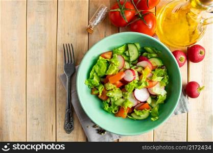 Fresh vegetable salad with olive oil in ceramic bowl on a wooden background. Seasonal summer dish of tomatoes, cucumbers and radishes. Place for text.. Fresh vegetable salad with olive oil in ceramic bowl on wooden background. Seasonal summer dish of tomatoes, cucumbers and radishes.