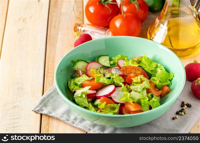 Fresh vegetable salad with olive oil in ceramic bowl on a wooden background. Seasonal summer dish of tomatoes, cucumbers and radishes. Place for text.. Fresh vegetable salad with olive oil in ceramic bowl on wooden background. Seasonal summer dish of tomatoes, cucumbers and radishes.