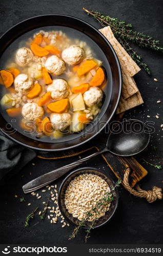 Fresh vegetable soup with meatballs and pearl barley in bowl on black background. Top view