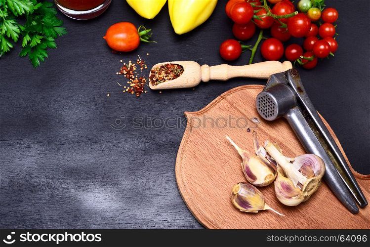 Fresh vegetables and garlic in the husk on a kitchen cutting board with a press for garlic