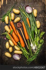 Fresh vegetables and herbs ingredients for cooking with old spoon on dark rustic wooden background, top view