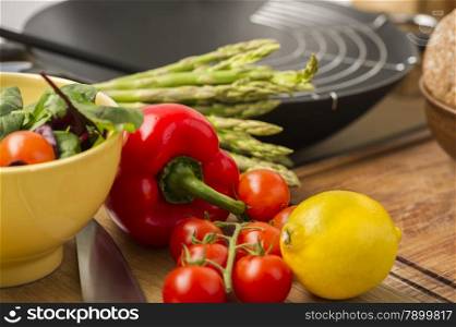 Fresh vegetables and salad ingredients on a wooden counter in a kitchen with cherry tomatoes, lemon, asparagus, red bell pepper and leafy herbs
