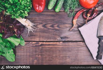 Fresh vegetables for salad on a brown wooden background, top view, empty place in the middle