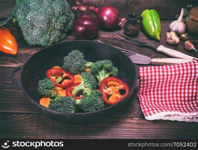 fresh vegetables in a black round frying pan on a brown wooden background, vintage toning