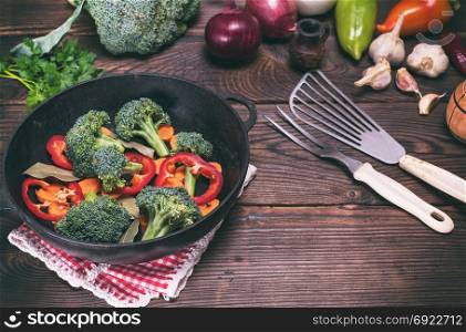 Fresh vegetables in a cast-iron black frying pan on a brown wooden background, vintage toning
