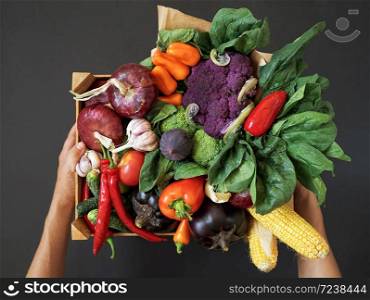 Fresh vegetables in a wooden box on a black background. Hands holding a box. Harvesting. Top view.
