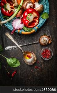 Fresh vegetables in basket, cooking spoons with oil and spices on rustic wooden background, top view. Vegetarian and Healthy food concept.