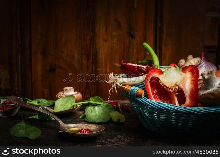 Fresh vegetables in blue basket , cooking spoon and ingredients on rustic kitchen table over wooden background. Healthy food concept.